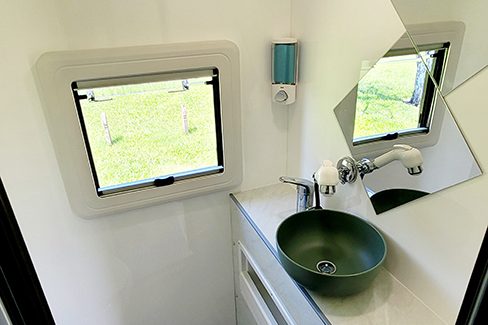 Bathroom of an Ozcape Slide-On with shower, toilet, vanity and window. Complete with shelf, mirror and soap dispenser.